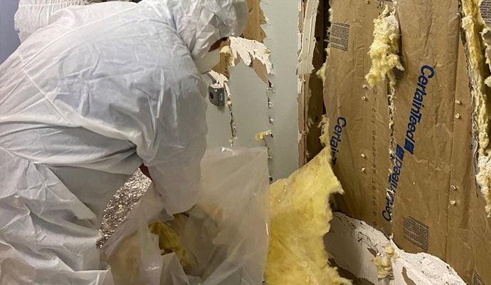 A technician in a hazmat suit removing insulation from a wall