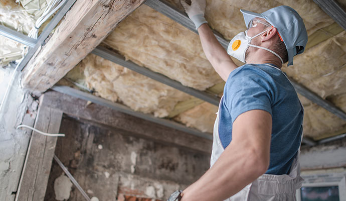 A technician in PPE installing insulation in a ceiling
