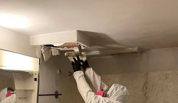 A technician removing ceiling drywall for smoke damage restoration