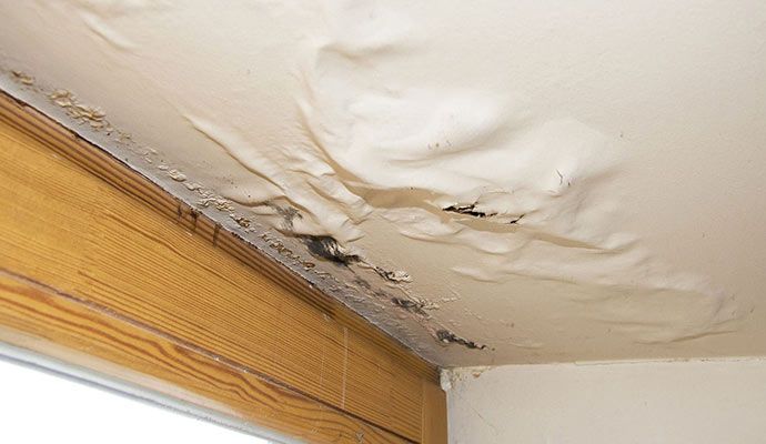 Damaged ceiling with visible water stains and peeling paint caused by a roof leak