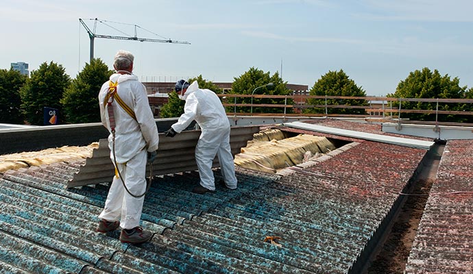 Experts in protective suits carefully removing asbestos roofing sheets from a building