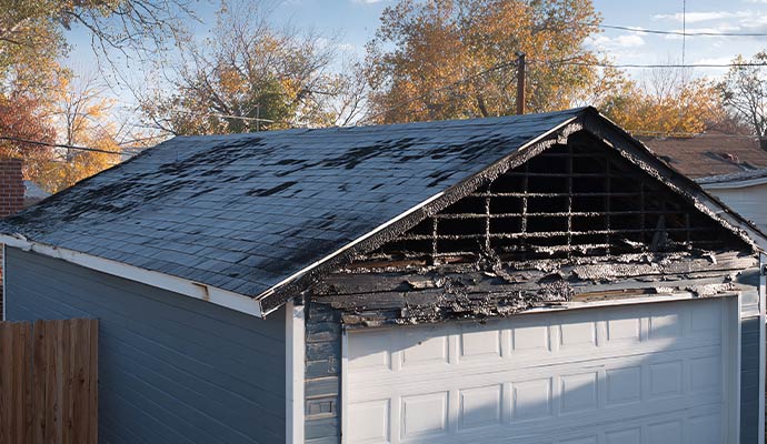 Fire damaged garage roof with charred wood exposed framing and burned siding from residential fire incident