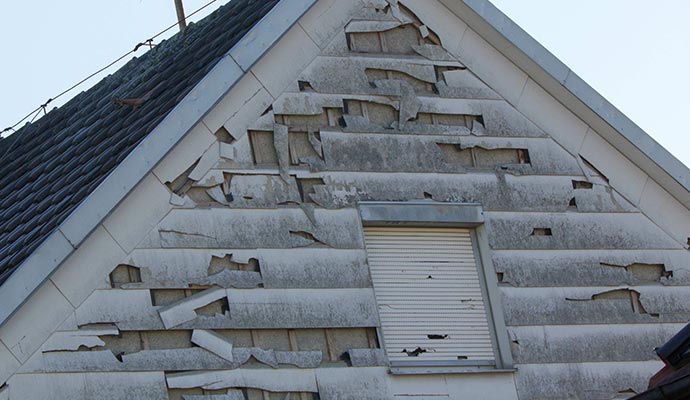 House siding damaged by hail, showing dents and broken exterior surfaces