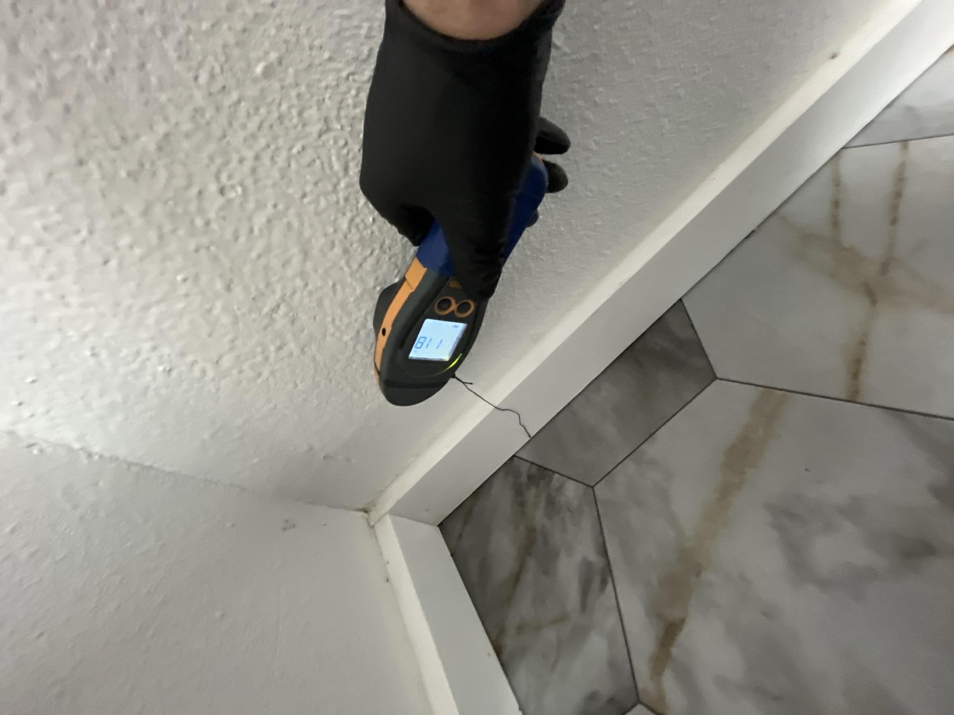 A professional technician using a moisture meter to detect water damage on a wall/baseboard, showing a reading of 118, confirming moisture intrusion under the sill plate for Alpha Omega Restoration Pros.