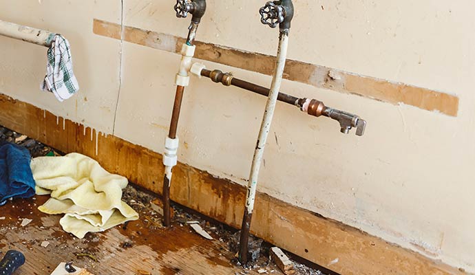 Leaking wall pipes causing water damage and stains near floor with visible corrosion and moisture buildup