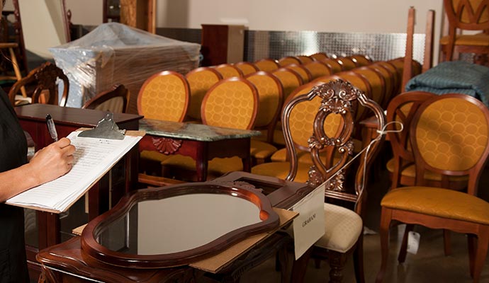 Person taking notes while inspecting restored furniture in a storage area
