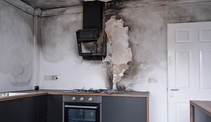Smoke damaged kitchen wall with soot stains burned range hood peeling paint and fire residue above stove area