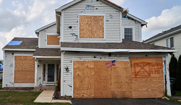 Storm-damaged two-story house with boarded-up windows and a boarded garage