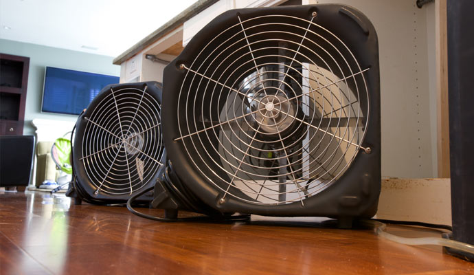 Two black air movers on a hardwood floor near kitchen cabinets